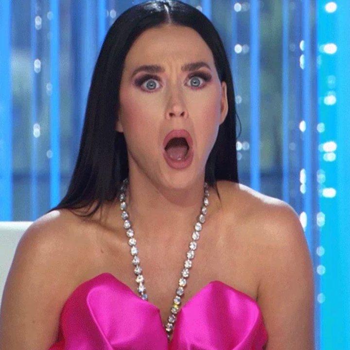 Person with long hair, wearing a strapless dress and necklace, appearing surprised or shocked