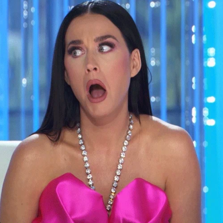 Person in a strapless dress with a dramatic facial expression, mouth open in surprise, seated against a background with vertical lines. 