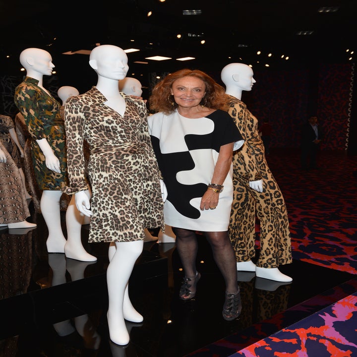 A woman stands with mannequins dressed in leopard print outfits at a fashion event, wearing a black and white patterned dress