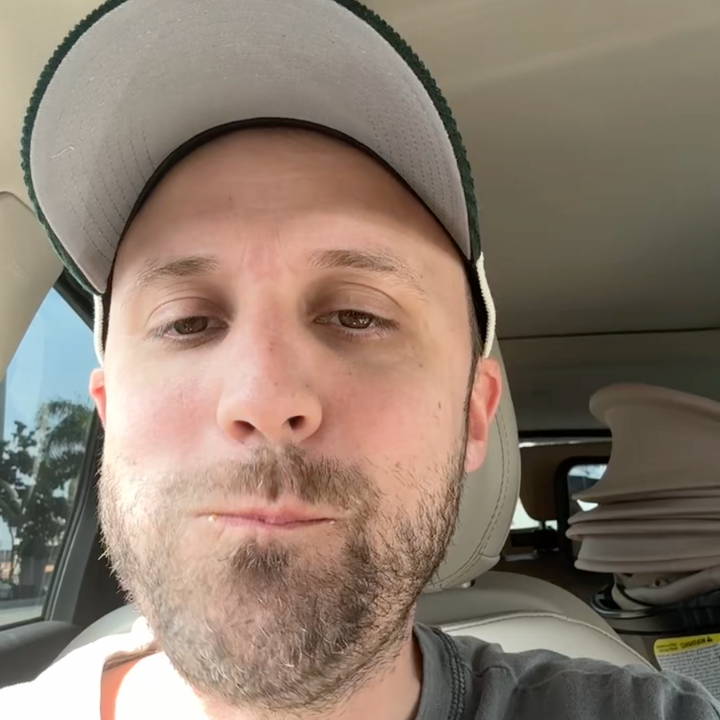 A man in a car appears to be eating or tasting something, with a thoughtful expression